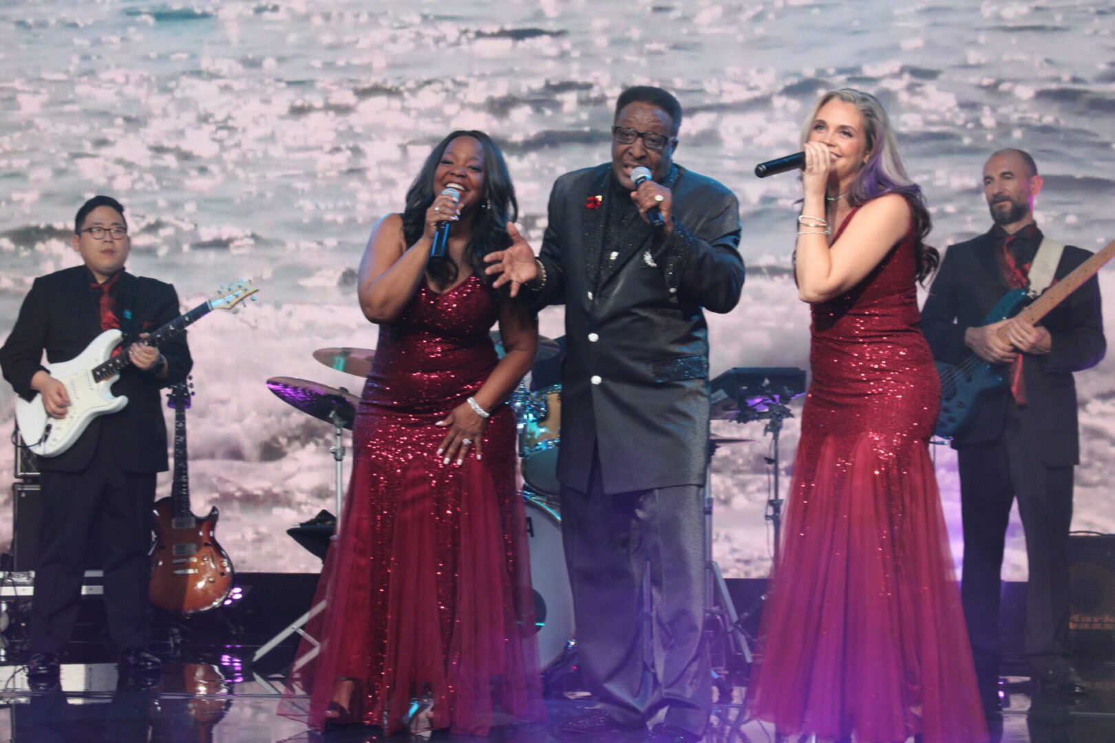 A group of people singing on stage with one man holding a microphone.